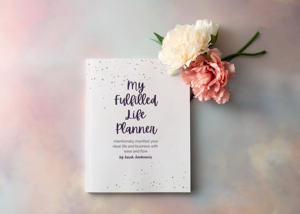 Flatlay of My Fulfilled Life Planner with a pink and cream flower at the top right of the image, on a soft focus background.